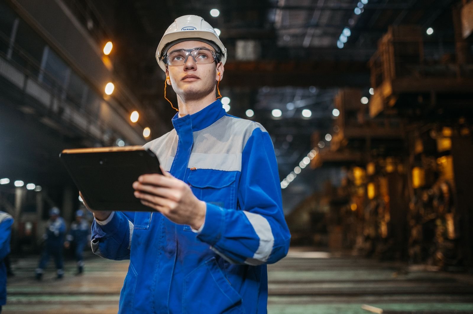 Engineer in safety gear using a tablet on a factory floor